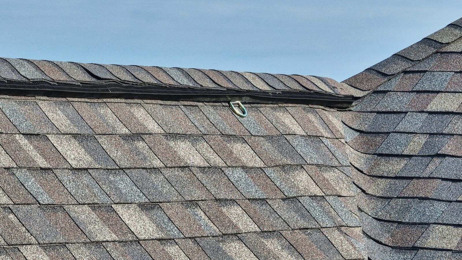 Close-up of a newly installed Multi-Family & Residential Roofing system with clean asphalt shingles, visible ridge vent, and hook attachment under a clear blue sky.