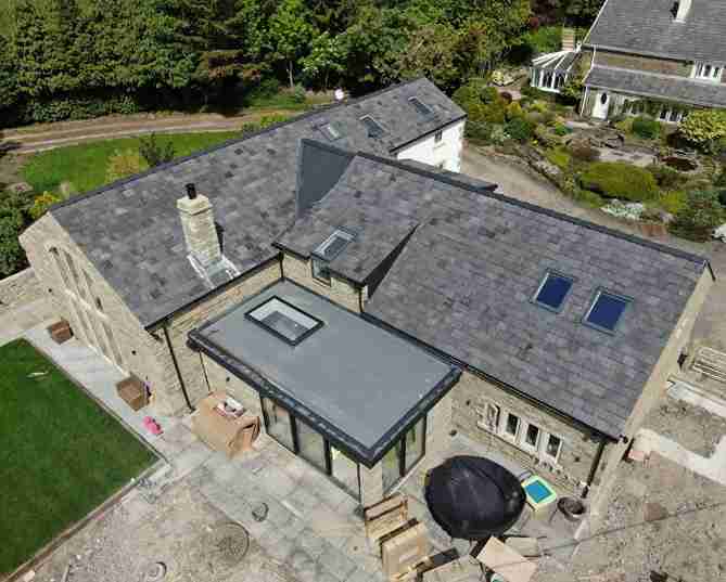 Residential home with new slate roof installation and flat roof extension with skylight.