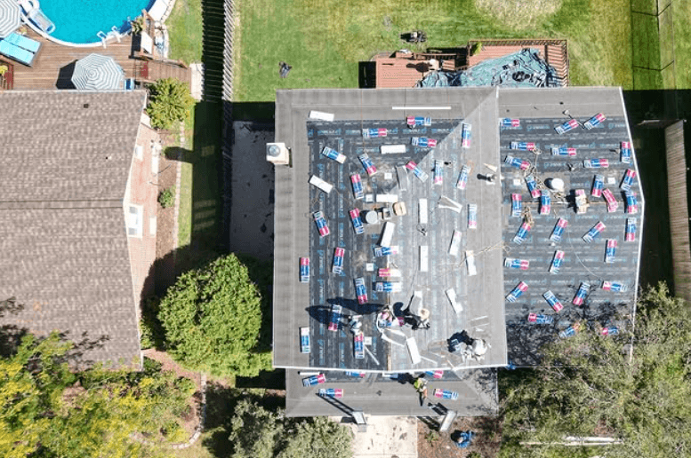 Aerial view of a commercial roof replacement in Paint Rock, TX with workers installing asphalt shingles and roofing materials.