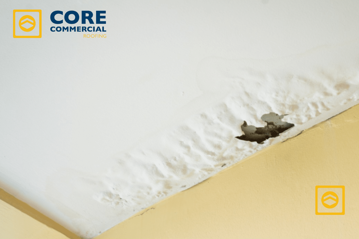 Water stain and peeling paint on a white ceiling due to a severe roof leak, with the Core Commercial Roofing logo visible.