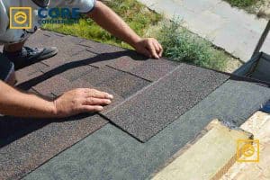 A professional roofer from Core Commercial Roofing completes a damaged roof repair by installing new asphalt shingles on a pitched commercial building.